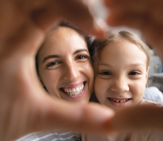 Smiling Hispanic Mom And Biracial Daughter Show Heart Sign